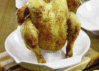 Romertopf vertical ceramic chicken roaster with a golden-brown whole roasted chicken on a wooden cutting board